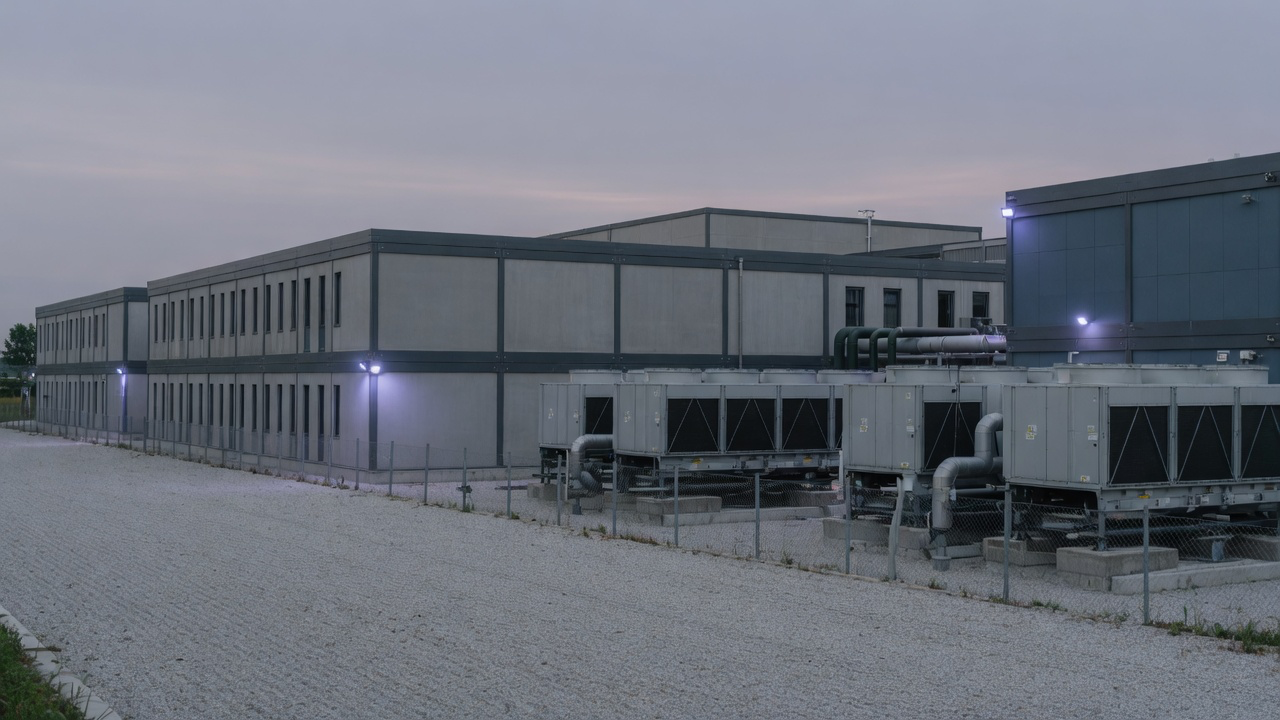 AI-generated editorial image: Exterior view of a modern European data center facility with clean architectural lines and modular cooling infrastructure at dusk.